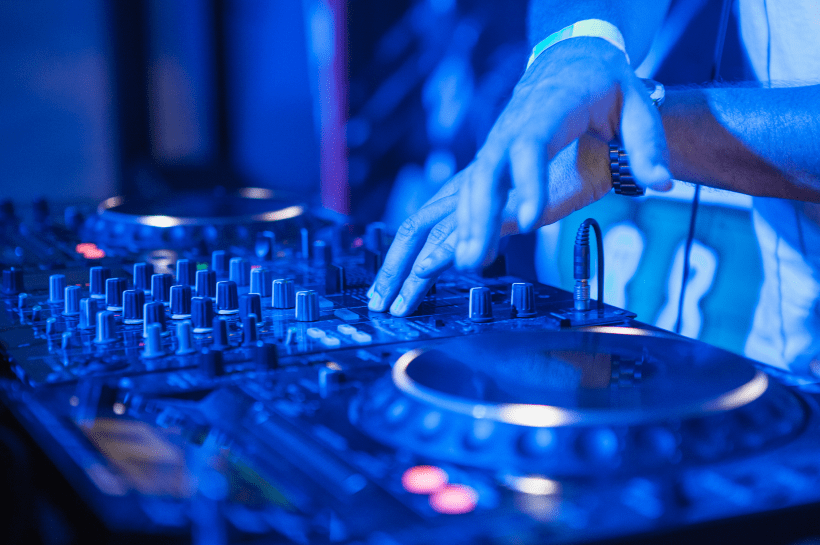 DJ operando mesa de mixagem com toca-discos e controles sob iluminação azul de casa noturna